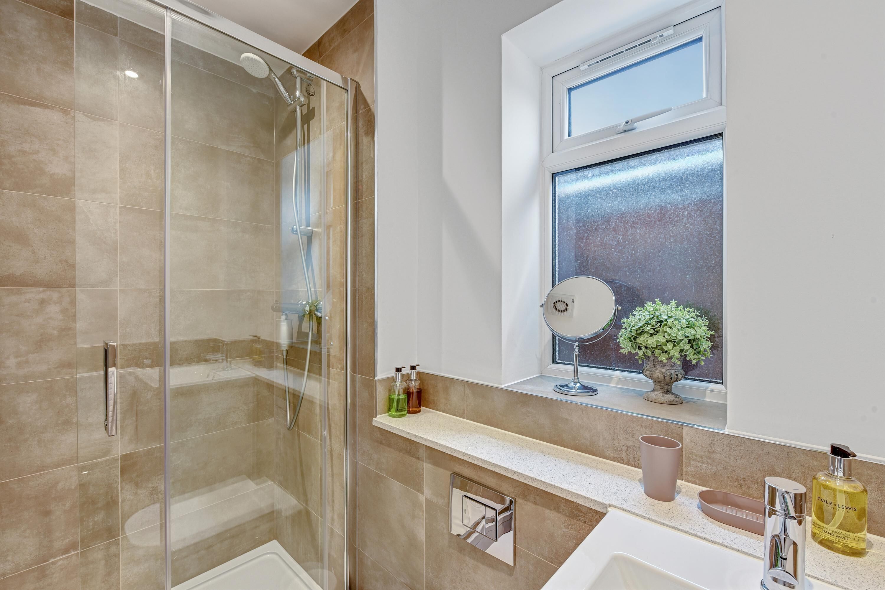 A modern bathroom with a glass-enclosed shower, a vanity with a mirror, and a window with a view.