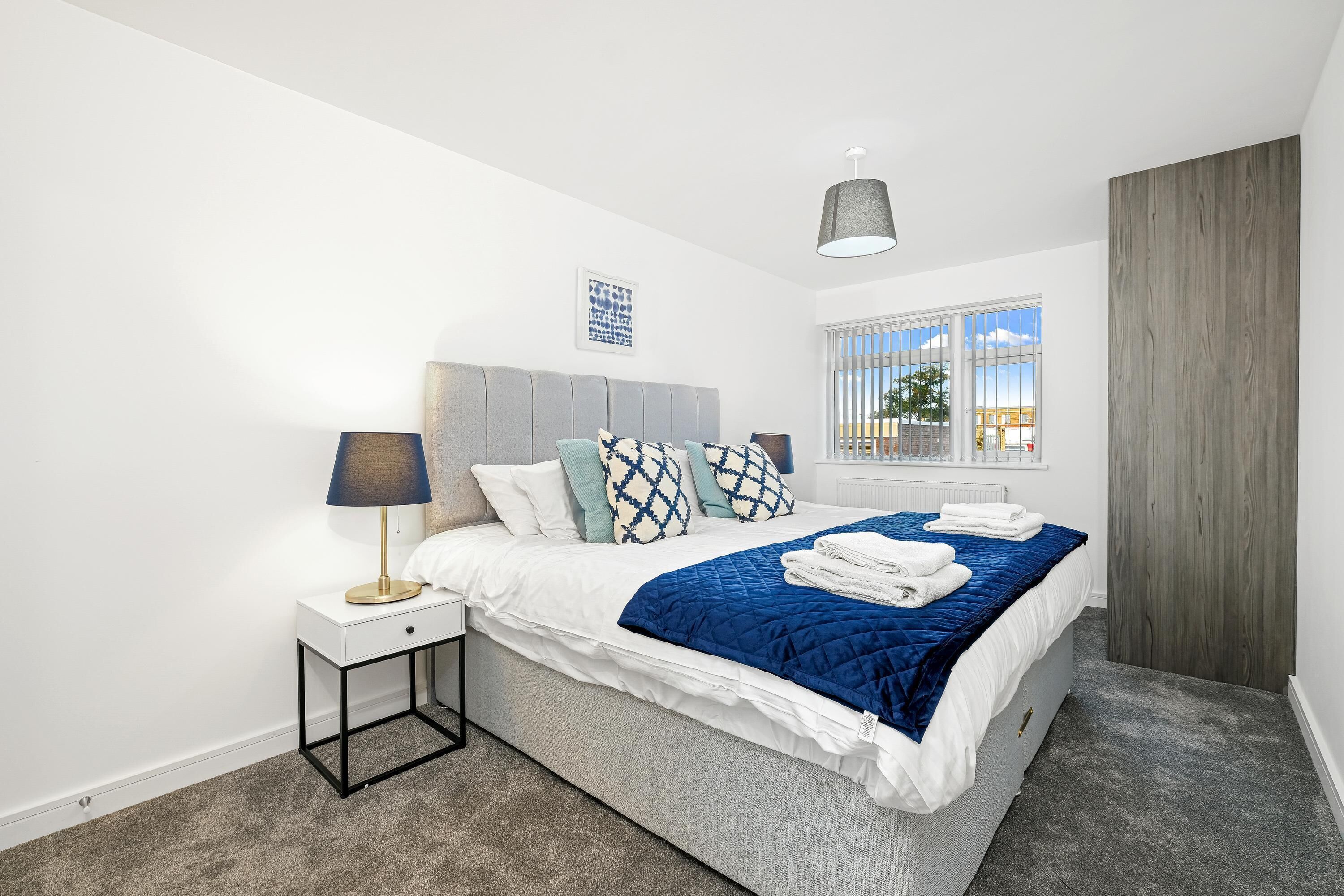 Ein modernes Schlafzimmer mit Bett, Nachttisch, Lampe und Fenster.