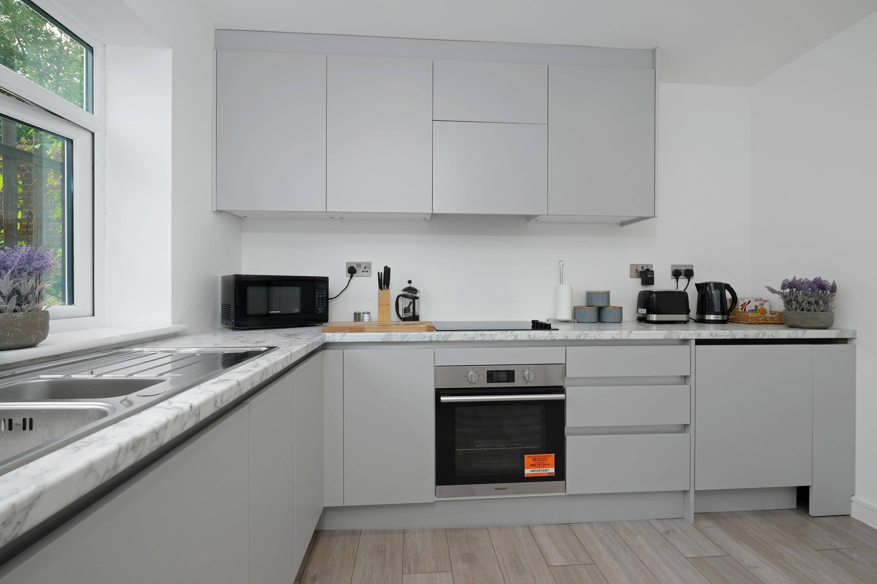 Une cuisine moderne avec des meubles blancs, un four encastré, un four à micro-ondes et une machine à café.