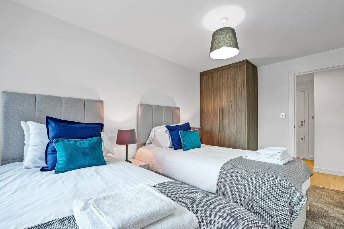 Una habitación de hotel moderna con dos camas, un armario de madera y una lámpara en el techo.