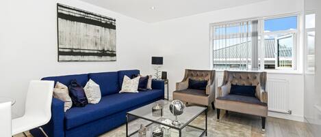 A modern living room with a blue sofa, a glass coffee table, and a brown armchair.