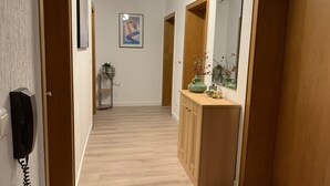 A hallway with wooden flooring, a telephone, a framed artwork, a plant, and a mirror on the wall.