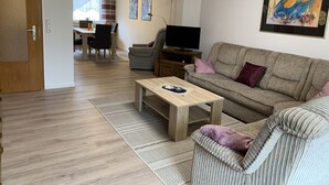 A living room with a sofa, a coffee table, a TV, and a dining area with a table and chairs.