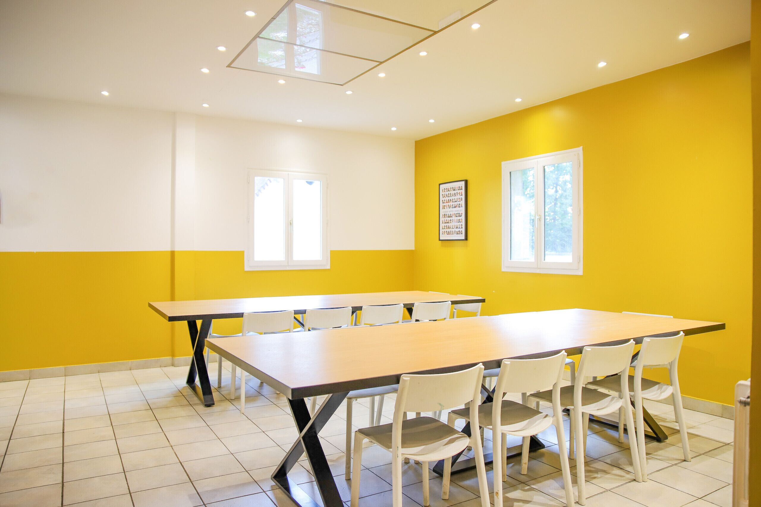 Een vergaderruimte met een lange tafel en stoelen, gele muren en ramen.