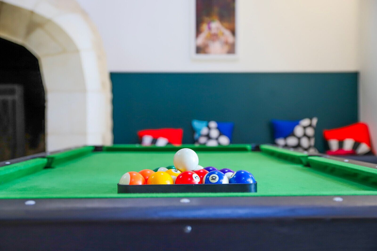 Ein Billardtisch mit Kugeln in der Mitte, einer grünen Spielmatte und einer weißen Wand im Hintergrund mit einem gerahmten Bild.