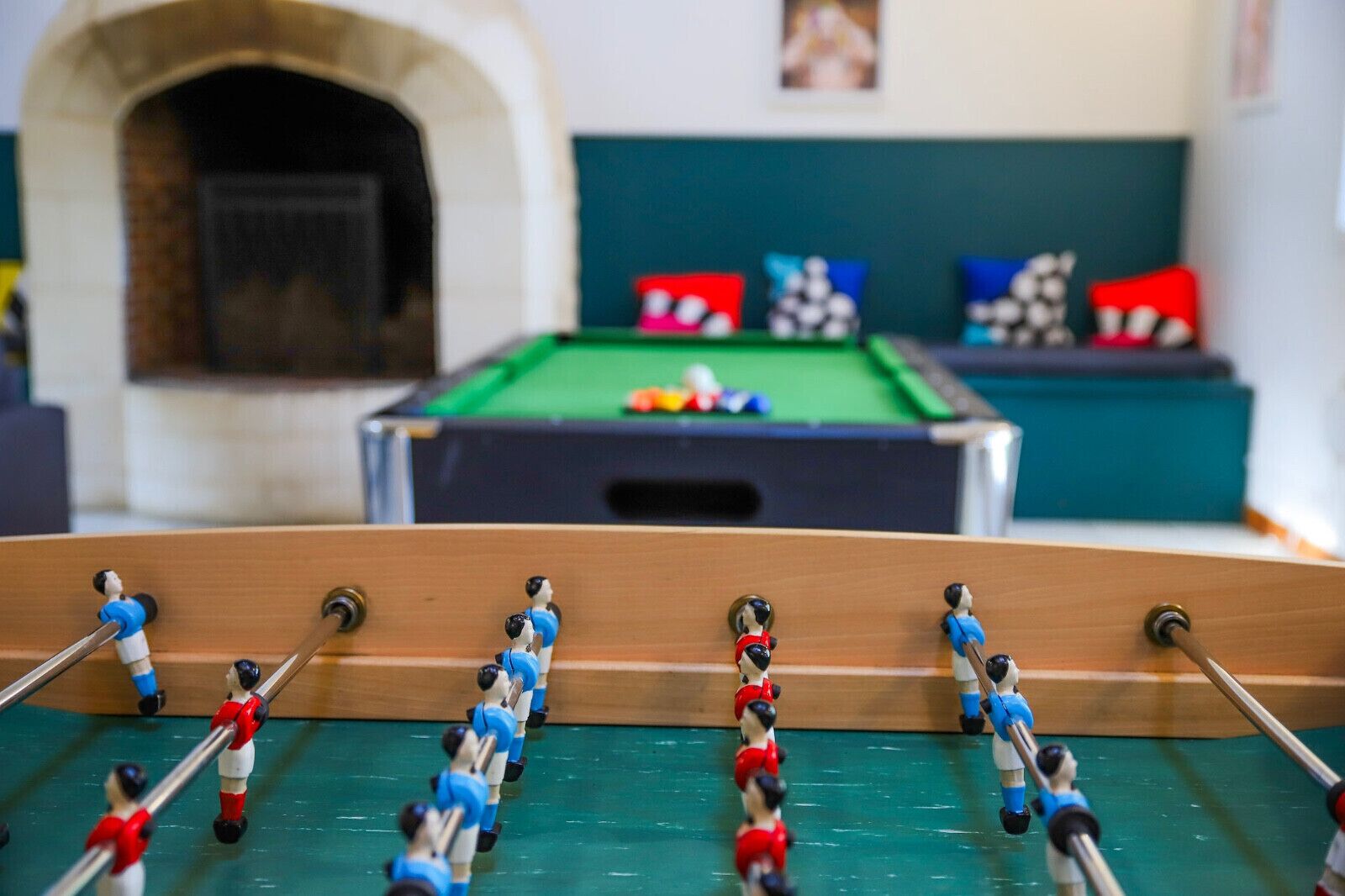 Een tafelvoetbaltafel in een kamer, met een biljarttafel op de achtergrond.