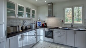 A modern kitchen with white cabinets, a stainless steel oven, and a window providing a view of trees. - Crazy Villa Ecottay (61) - Heated pool - 2h from Paris - 30p. (Longny les Villages)