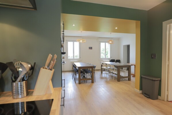A spacious dining area with a long wooden table and chairs, a kitchen area with a sink and utensils, and a trash bin. - Crazy Villa Radar (89) - Heated pool - Multisports field - 2h Paris - 30p. (Saint-Cyr-les-Colons)