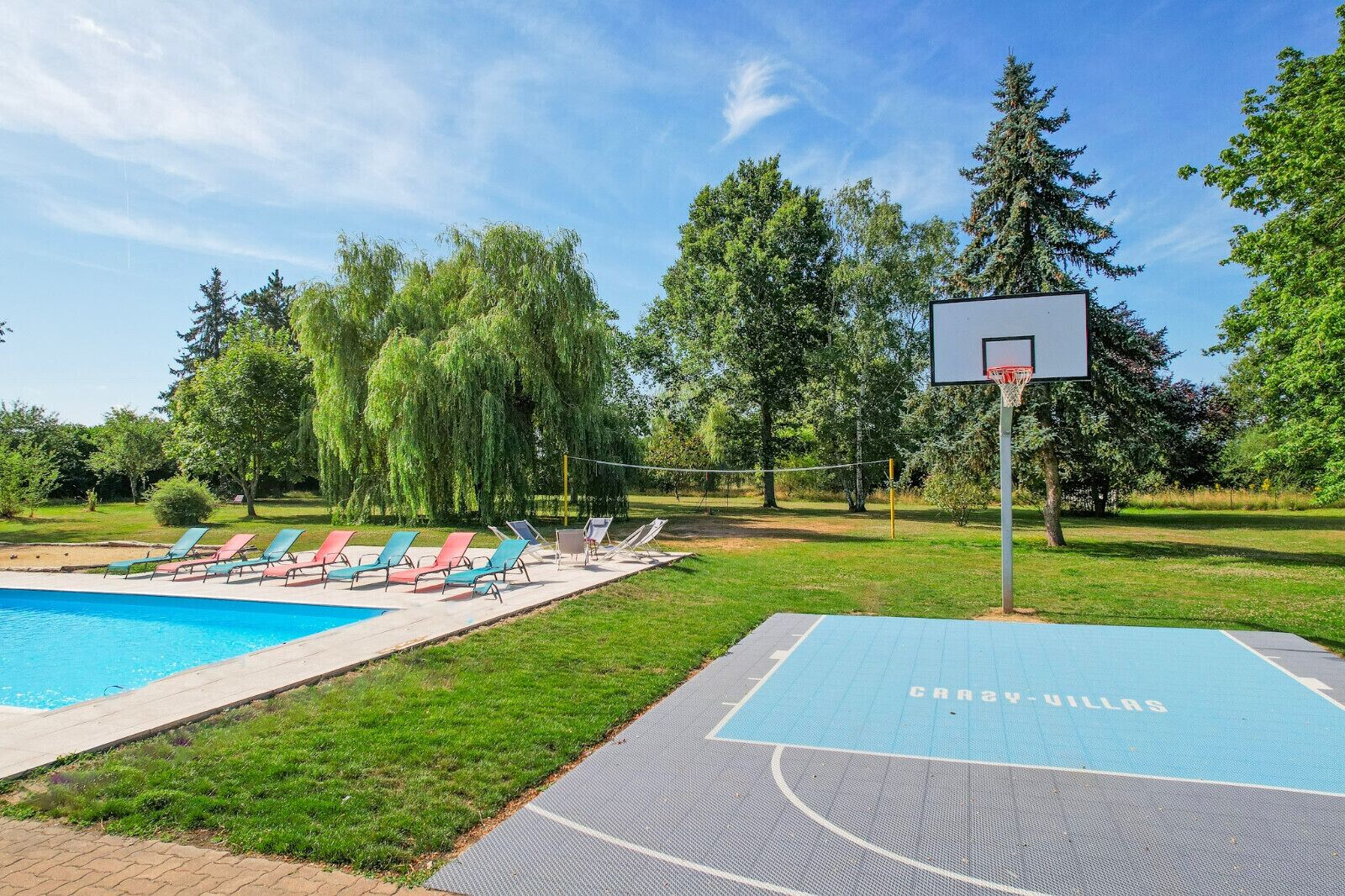 Une piscine avec des chaises longues et un terrain de basket.