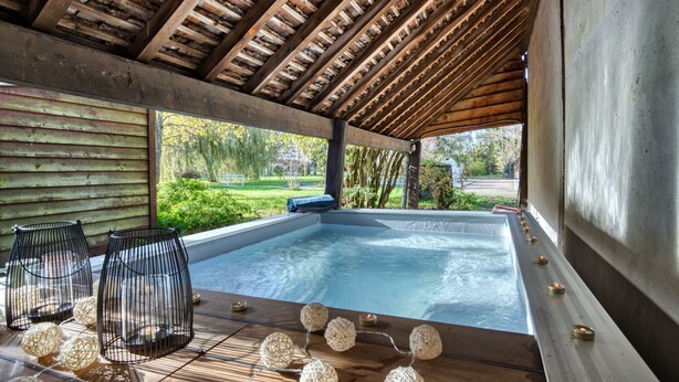 Una piscina al aire libre techada con vigas de madera, asientos y luces decorativas.