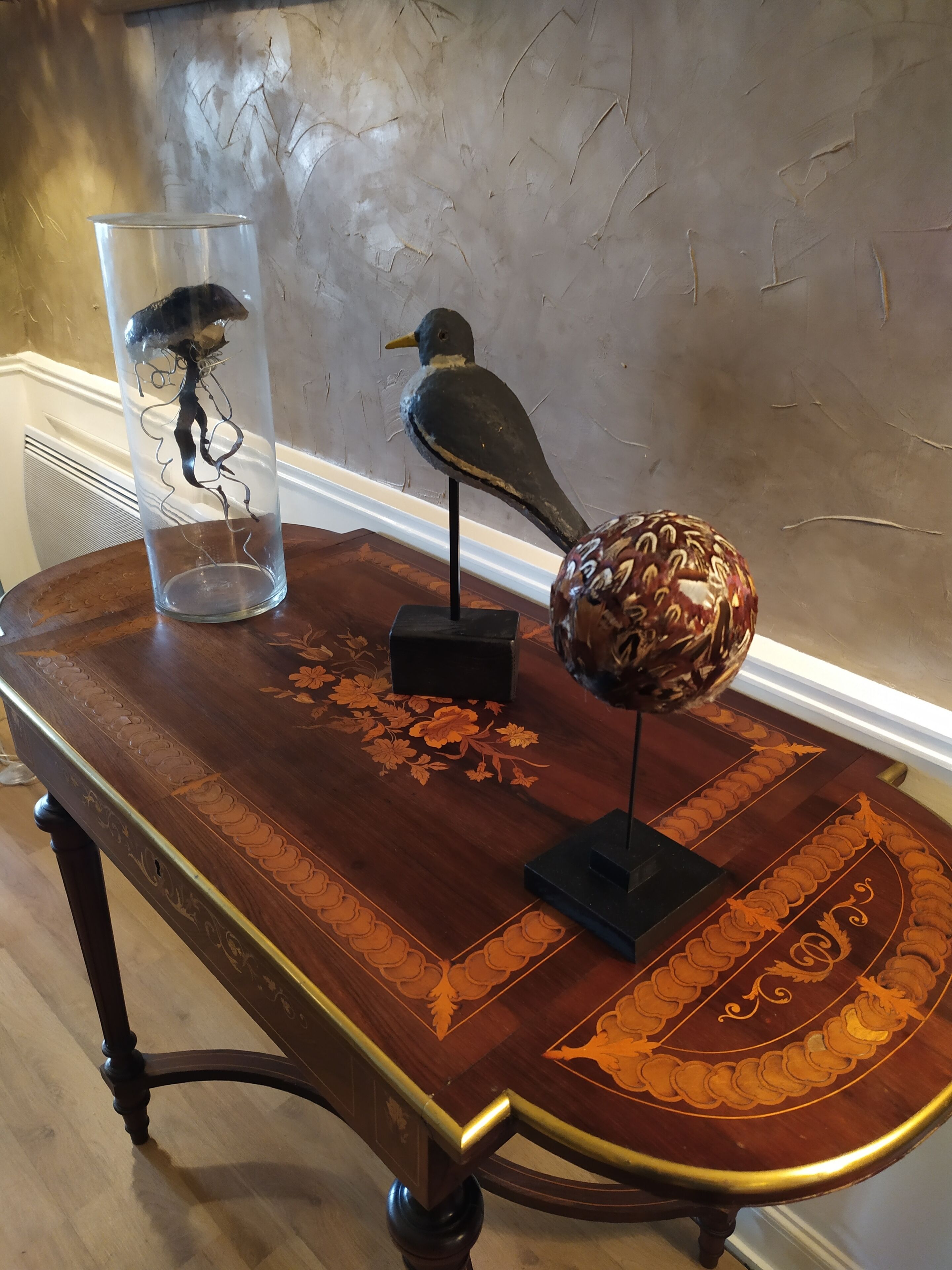 A wooden table with a glass vase containing a bird and a decorative sphere.