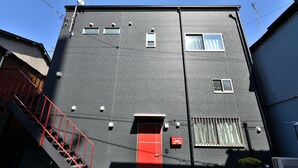 Ein zweistöckiges Gebäude mit roter Tür, einem kleinen Fenster und einer roten Treppe.