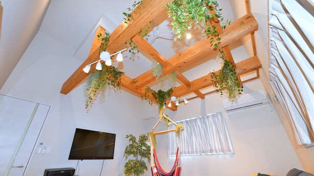 Ein Wohnzimmer mit Holzboden, einem an der Wand montierten Fernseher, einer Couch und einer Hängematte.
