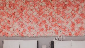 Ein Schlafzimmer mit zwei Betten, weißer Bettwäsche, einem Nachttisch mit Lampe und einer Blumen-Wanddekoration.