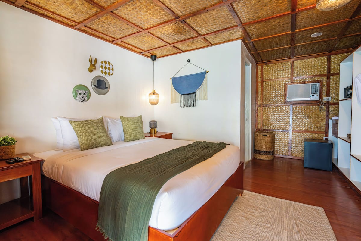 A bedroom with a bed, bedside tables, a hanging light fixture, and a woven ceiling.