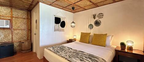 A bedroom with a large bed, wooden beams, a woven ceiling, and a nightstand with a lamp.
