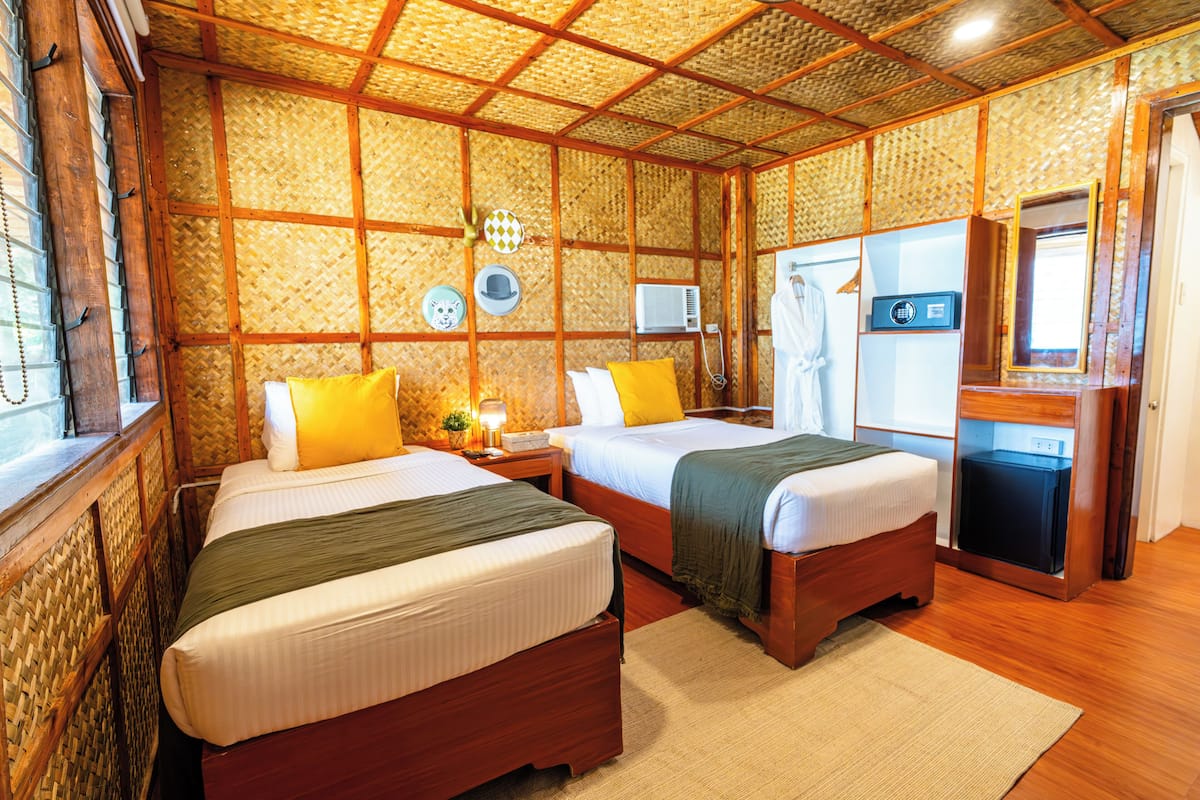 A room with two beds, wooden walls, a small table, a mirror, and a window.