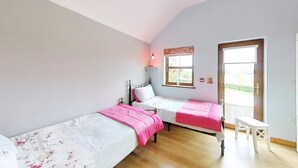 Una camera da letto con due letti singoli, pavimento in legno, una finestra vista e un piccolo tavolo.