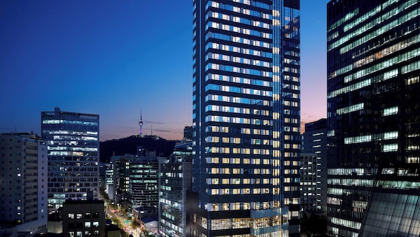 Un edificio de gran altura con fachada de vidrio moderna, varios pisos y ventanas iluminadas.