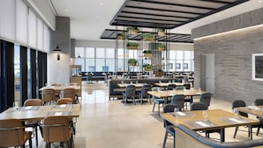 Un comedor moderno con mesas largas y cabinas, ventanas amplias y plantas colgantes.