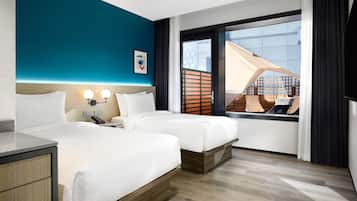 A hotel room with two beds, a desk, a phone, and a window with a view of a building.