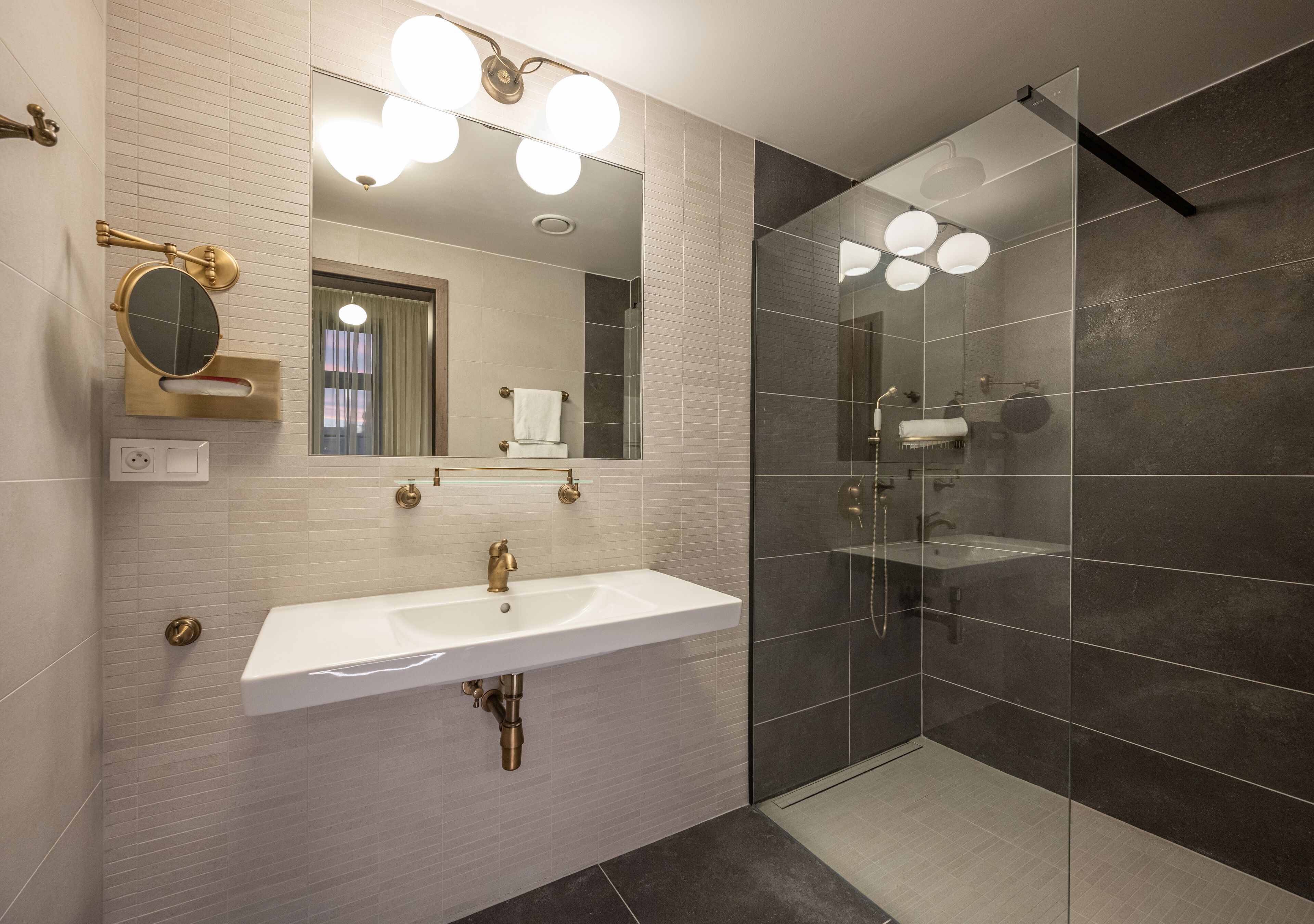 A modern bathroom with a white sink, gold fixtures, and a glass-enclosed shower.