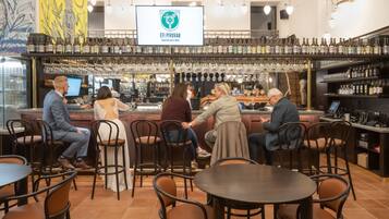 Una zona de bar con diferentes opciones de asientos, una exhibición de botellas de vino y una pantalla digital.