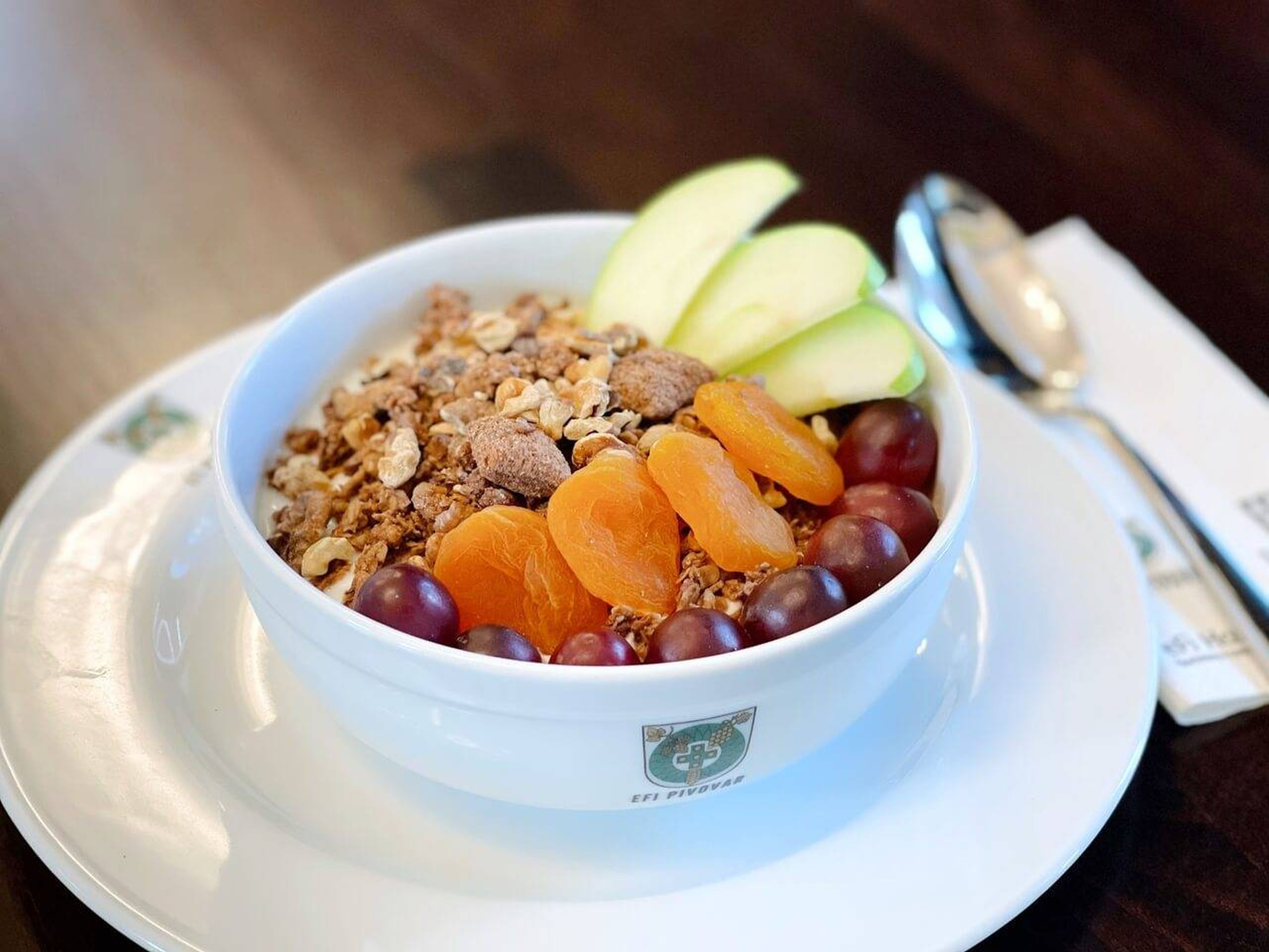 A bowl of cereal with fruits and nuts on a white plate.