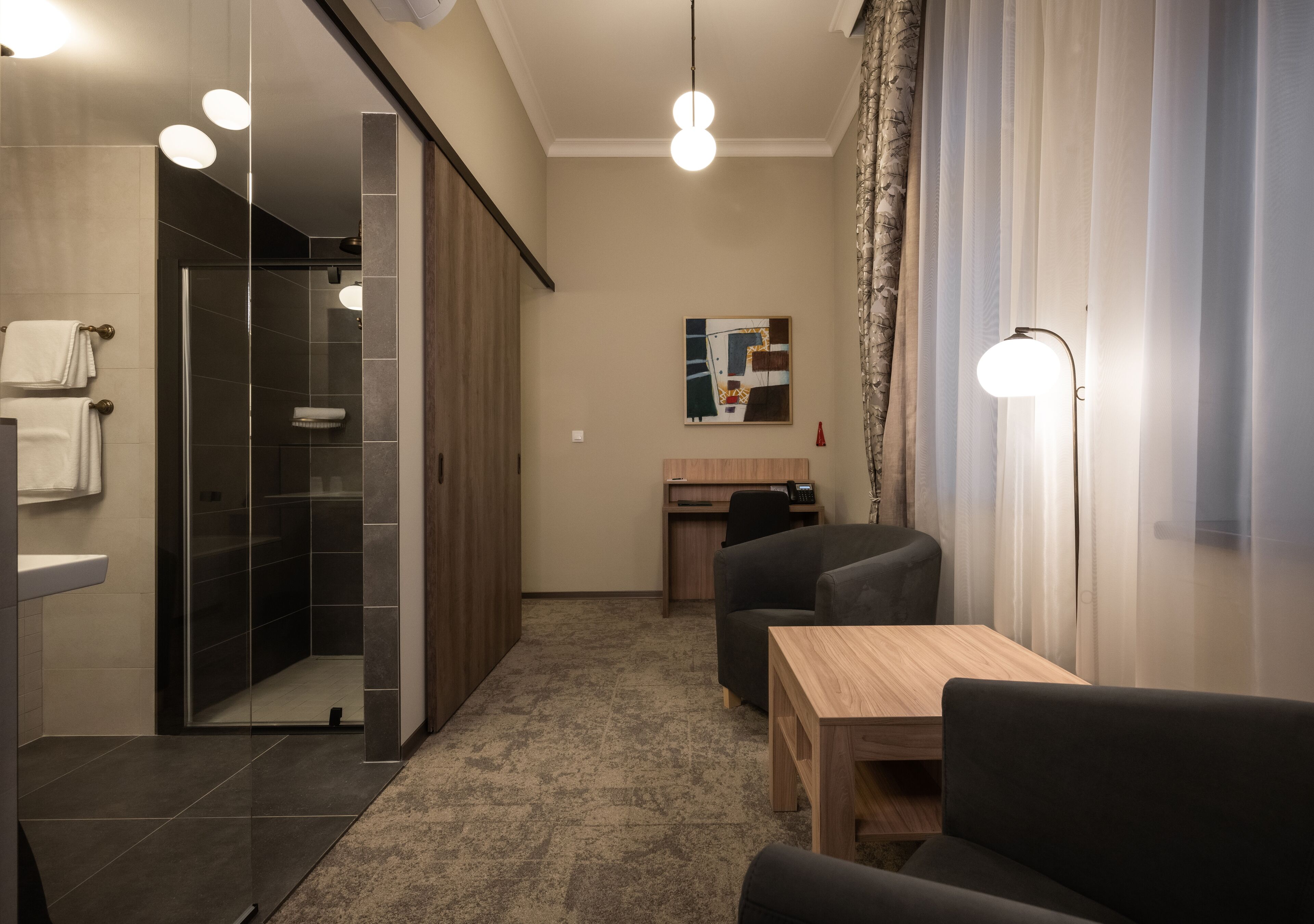 Ett modernt hotellrum med dusch, skrivbord och en sittgrupp.