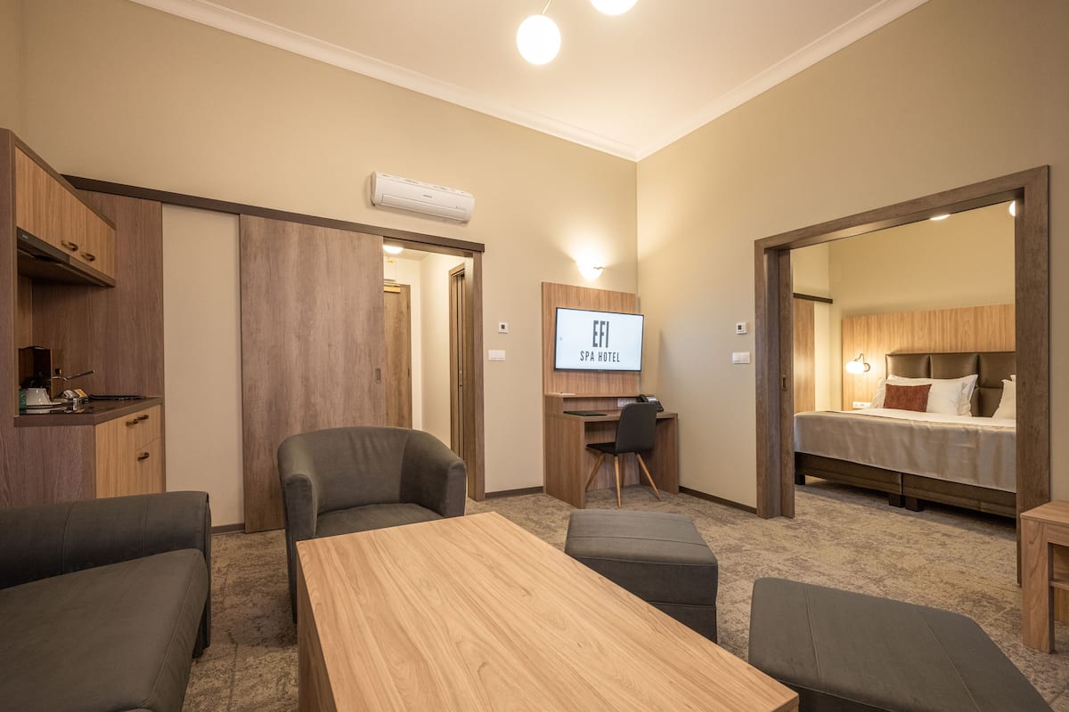 A hotel room with a wooden desk, two armchairs, a sofa, a bed, and a TV displaying "EFI SPA HOTEL".