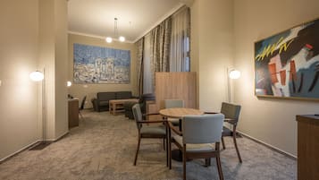 Una habitación de hotel moderna con una mesa de comedor redonda, dos sillas, un sofá y un cuadro abstracto grande en la pared.