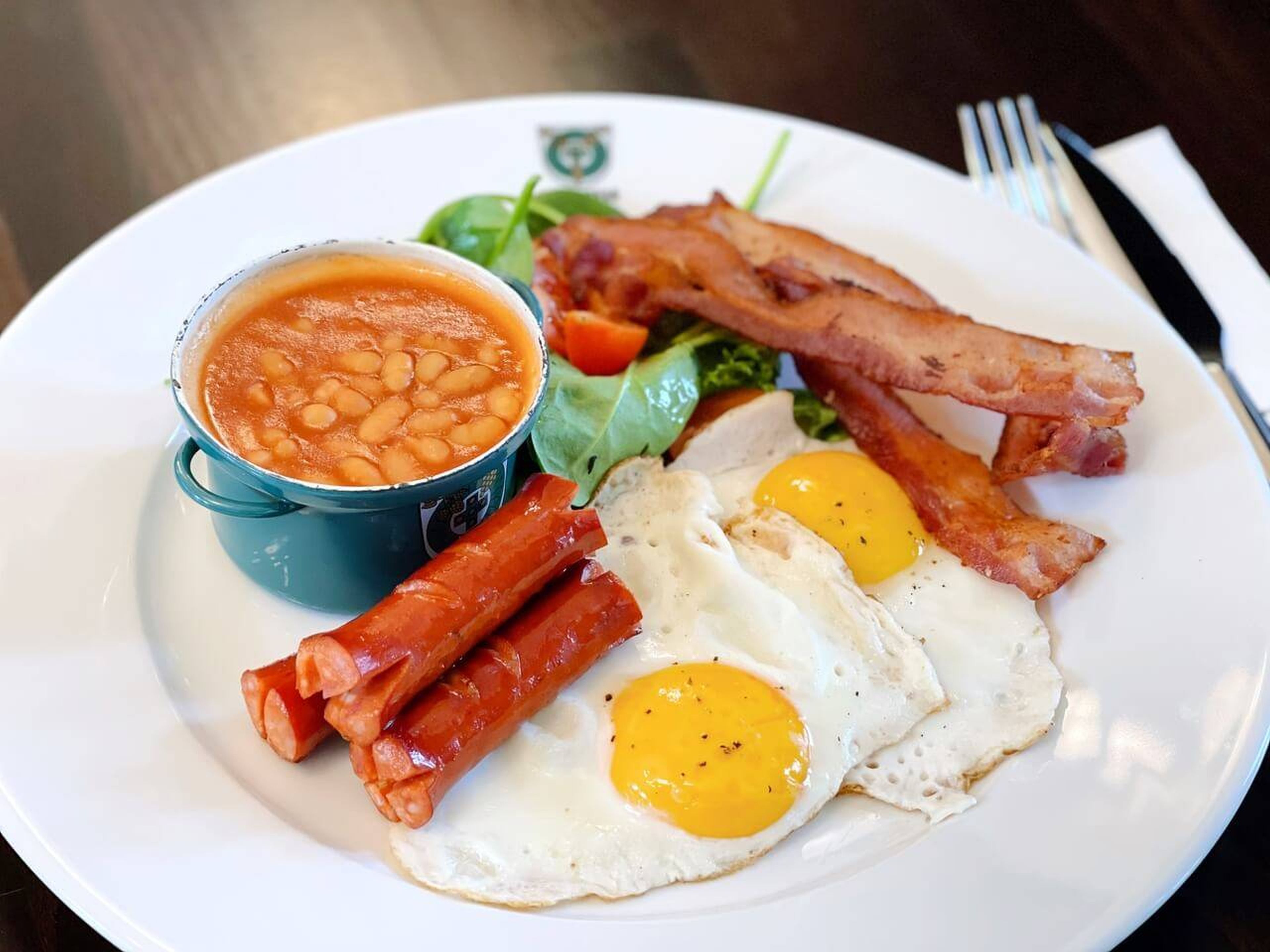 Un plato con frijoles, tocino, huevos y una ensalada pequeña.