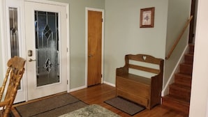 A hallway with a wooden bench, a door with a glass panel, and a staircase.