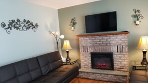 A living room with a brick fireplace, a black leather sofa, and two wall-mounted lamps.