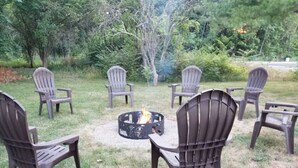 A circular fire pit with chairs arranged around it in a grassy outdoor area.
