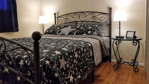 A neatly made bed with a star-patterned bedspread, two bedside lamps, and a small table with a lamp and a framed picture.