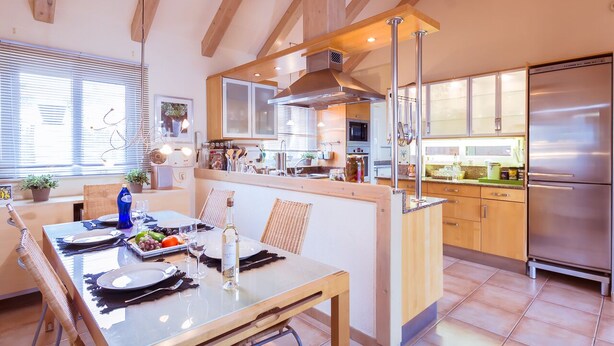A modern kitchen with wooden beams, a central island, stainless steel appliances, and a dining area with a table set for two.