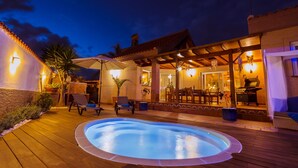 A pool area with a hot tub, lounge chairs, and a covered patio with a dining table and chairs.