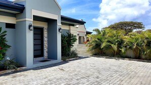 Una casa moderna con entrada pavimentada, pared de piedra decorativa y plantas tropicales.