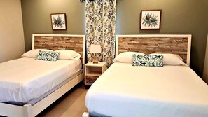 Two single beds with wooden headboards and white bedding, accompanied by two nightstands with lamps and small tables, and framed botanical prints on the walls.