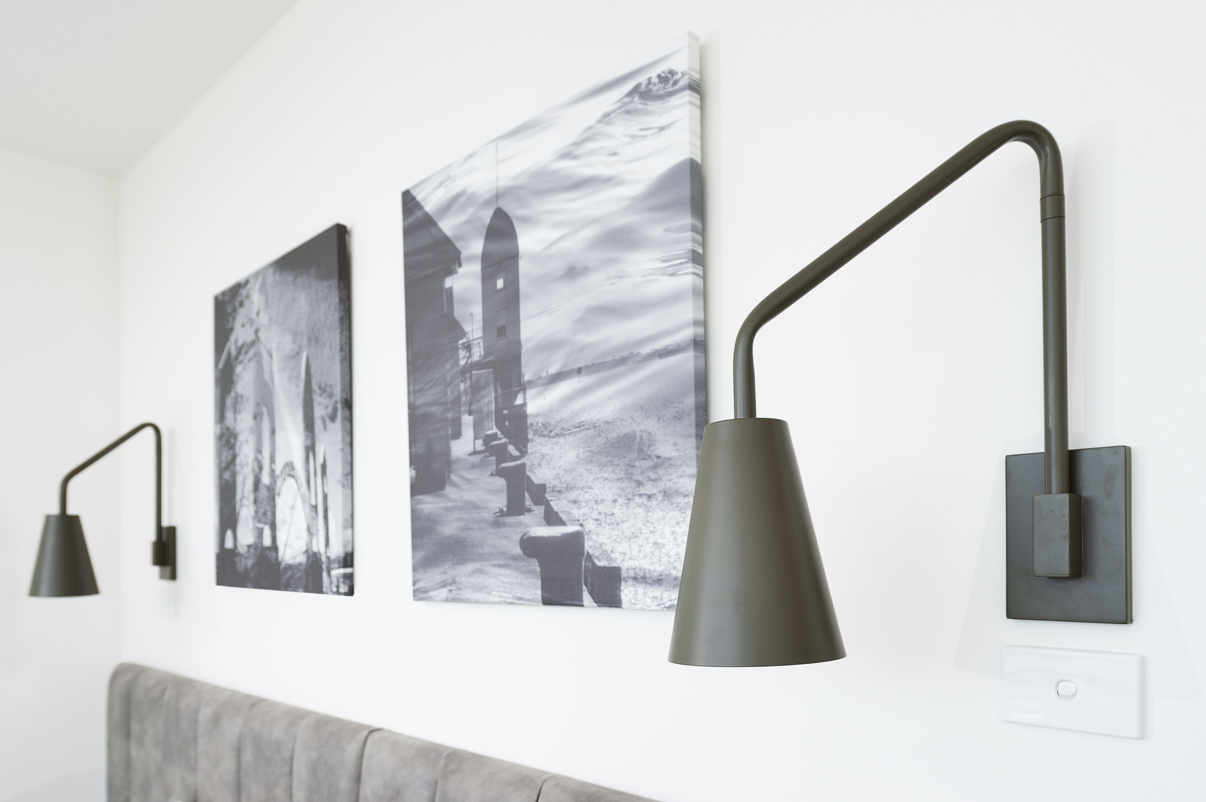 Eine Wand mit drei schwarzen Wandlampen und zwei Schwarz-Weiß-Fotografien.
