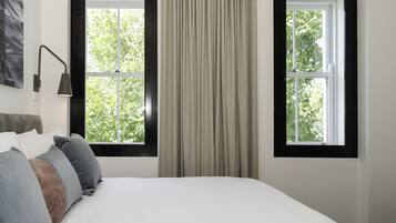 A bedroom with a bed, two windows, a lamp, and a painting on the wall.