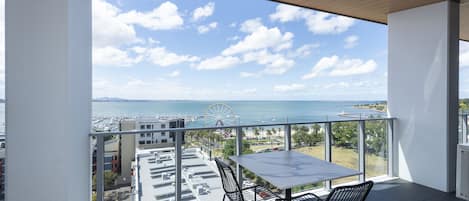 A balcony with a table and chairs, overlooking a marina and a Ferris wheel.