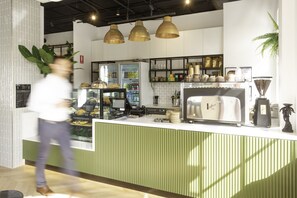A modern cafe interior with a counter, coffee machines, and shelves stocked with pastries and beverages.