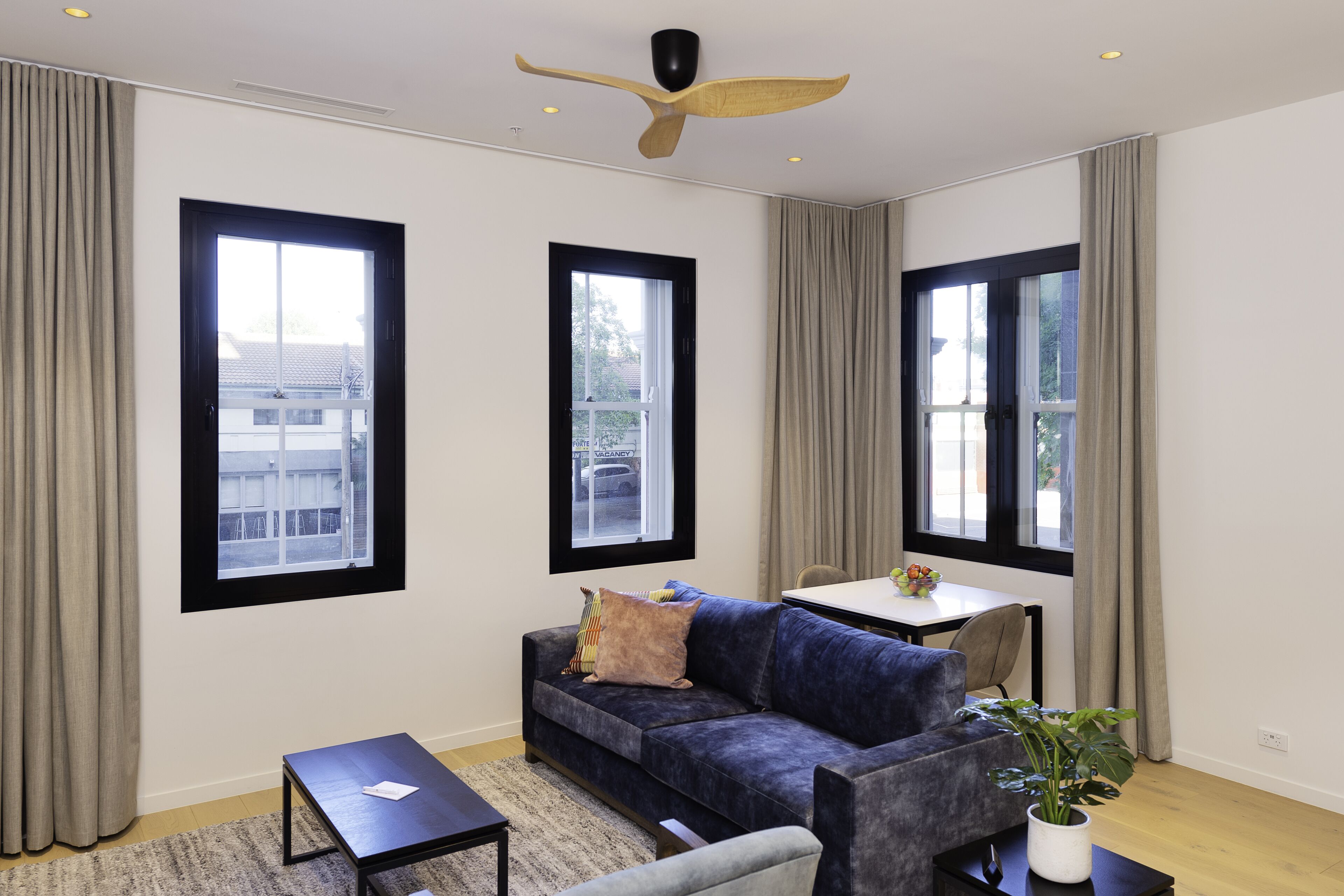 A modern living room with a dark blue sofa, a small table, and a ceiling fan.