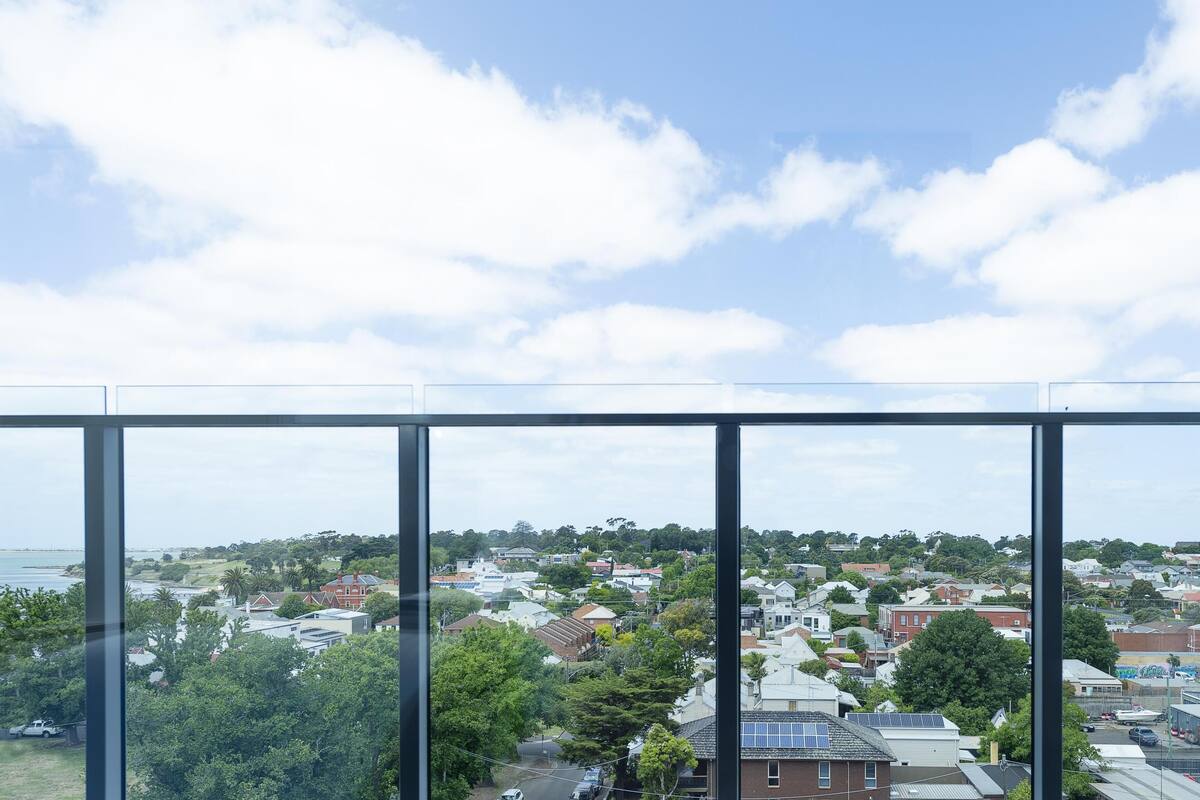 A view from a high-rise building with large windows overlooking a residential area with houses, trees, and a body of water.
