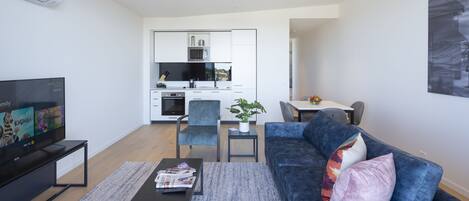 A modern living room with a TV, sofa, coffee table, and a small dining area with a plant.