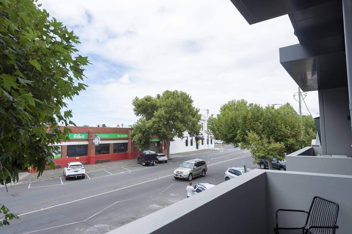 A street view with a building featuring a green sign, a parking lot, and a few cars.