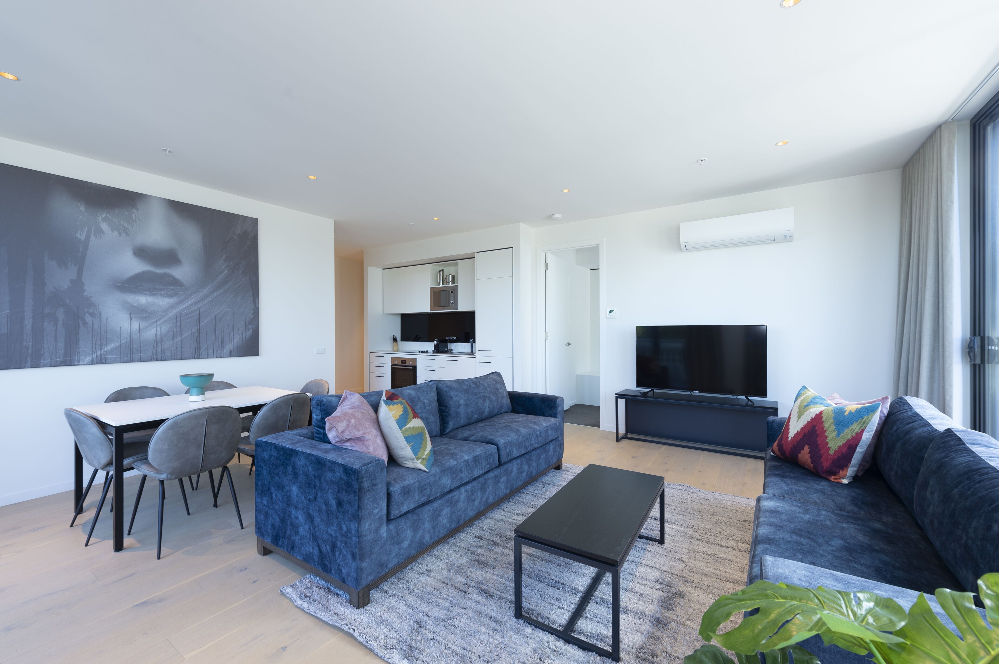 A modern living room with a blue sofa, a coffee table, and a dining area with chairs and a table.