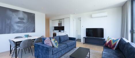 A modern living room with a blue sofa, a coffee table, and a dining area with chairs and a table.